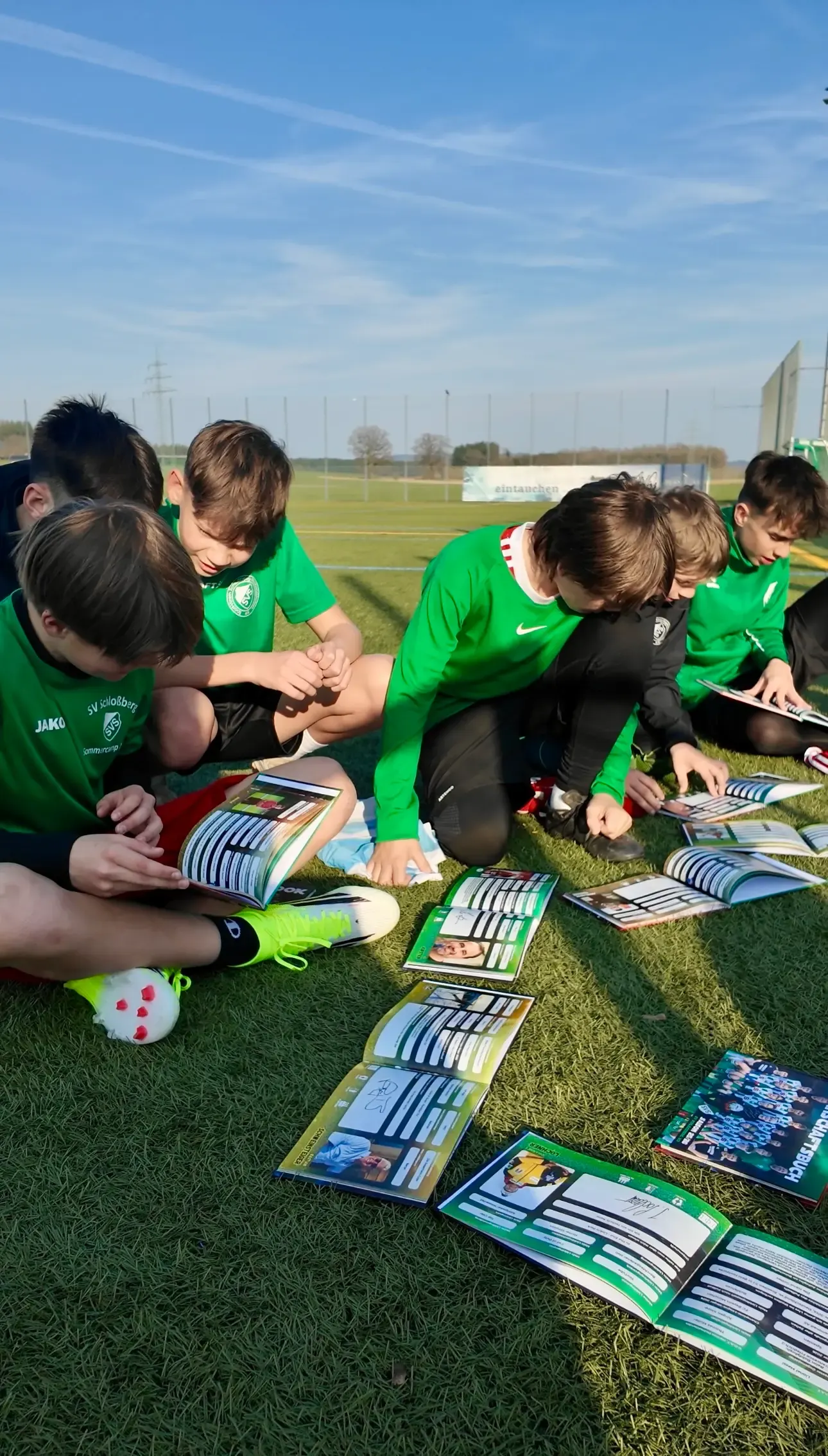 Kinderteam in grünen Trikots liest Flashbooks auf dem Rasen